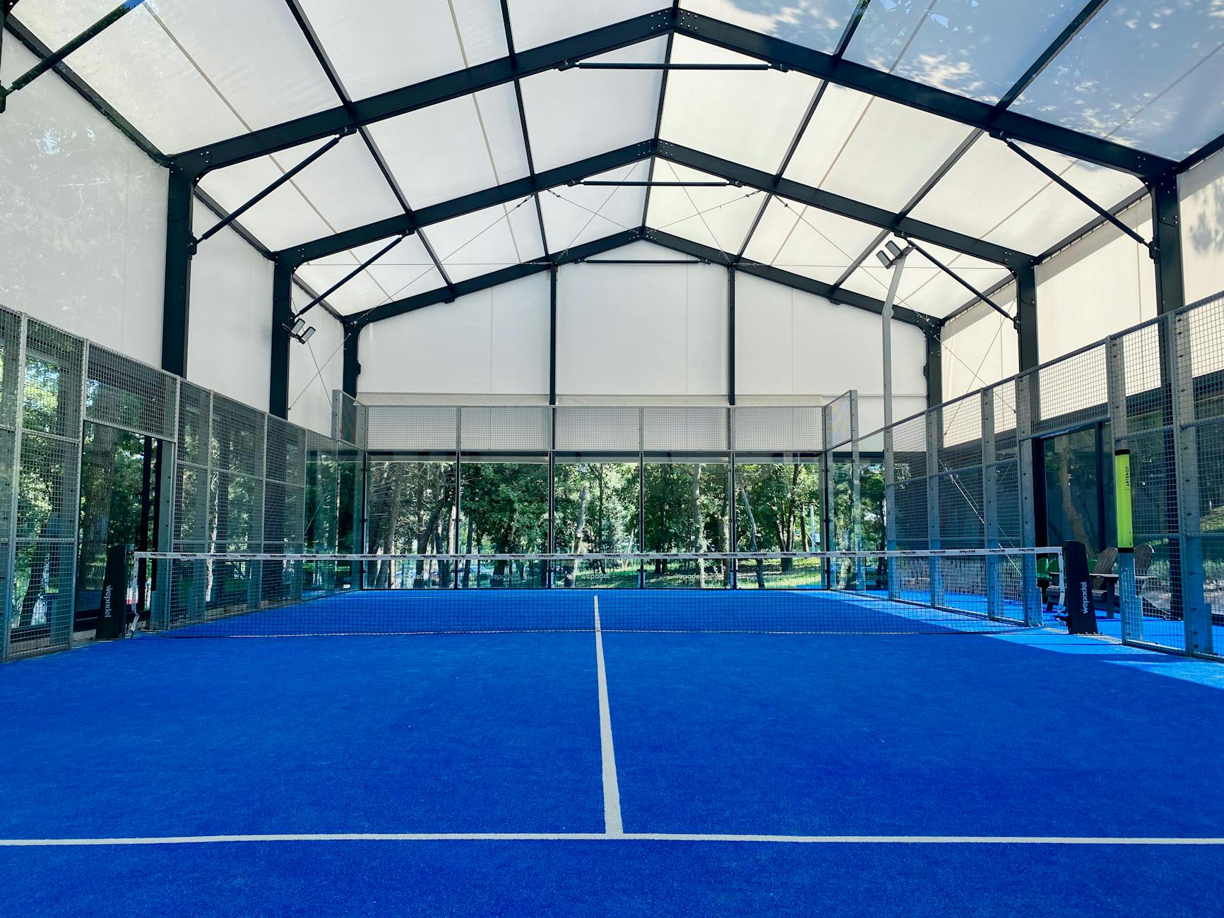 Campo de padel interior vazio com piso azul e cobertura ampla